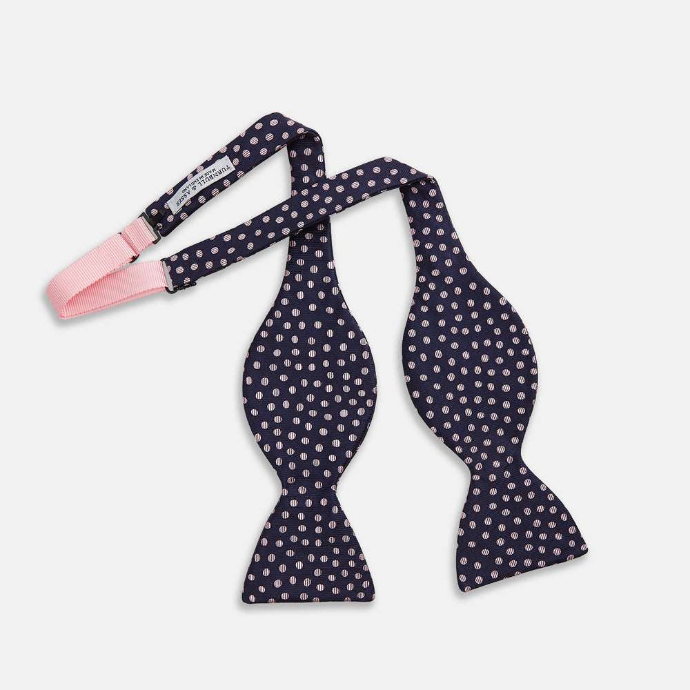 The Navy and Pink Paint Spot Silk Bow Tie by Turnbull & Asser features small, light pink oval dots evenly spaced on navy blue silk, creating a stylish formal accessory.