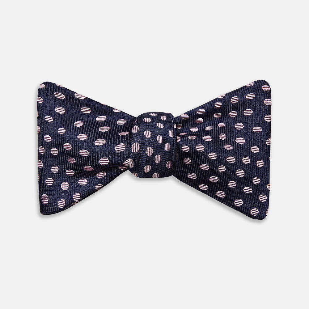 The Navy and Pink Paint Spot Silk Bow Tie by Turnbull & Asser features small, light pink oval dots evenly spaced on navy blue silk, creating a stylish formal accessory.