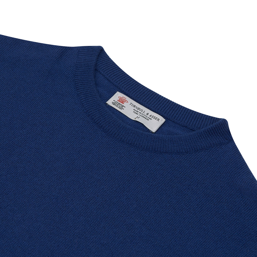 The Turnbull & Asser Blue Crew Neck Cashmere Jumper, neatly folded with ribbed collar and cuffs, is shown on a plain white background. A small label appears inside the collar.