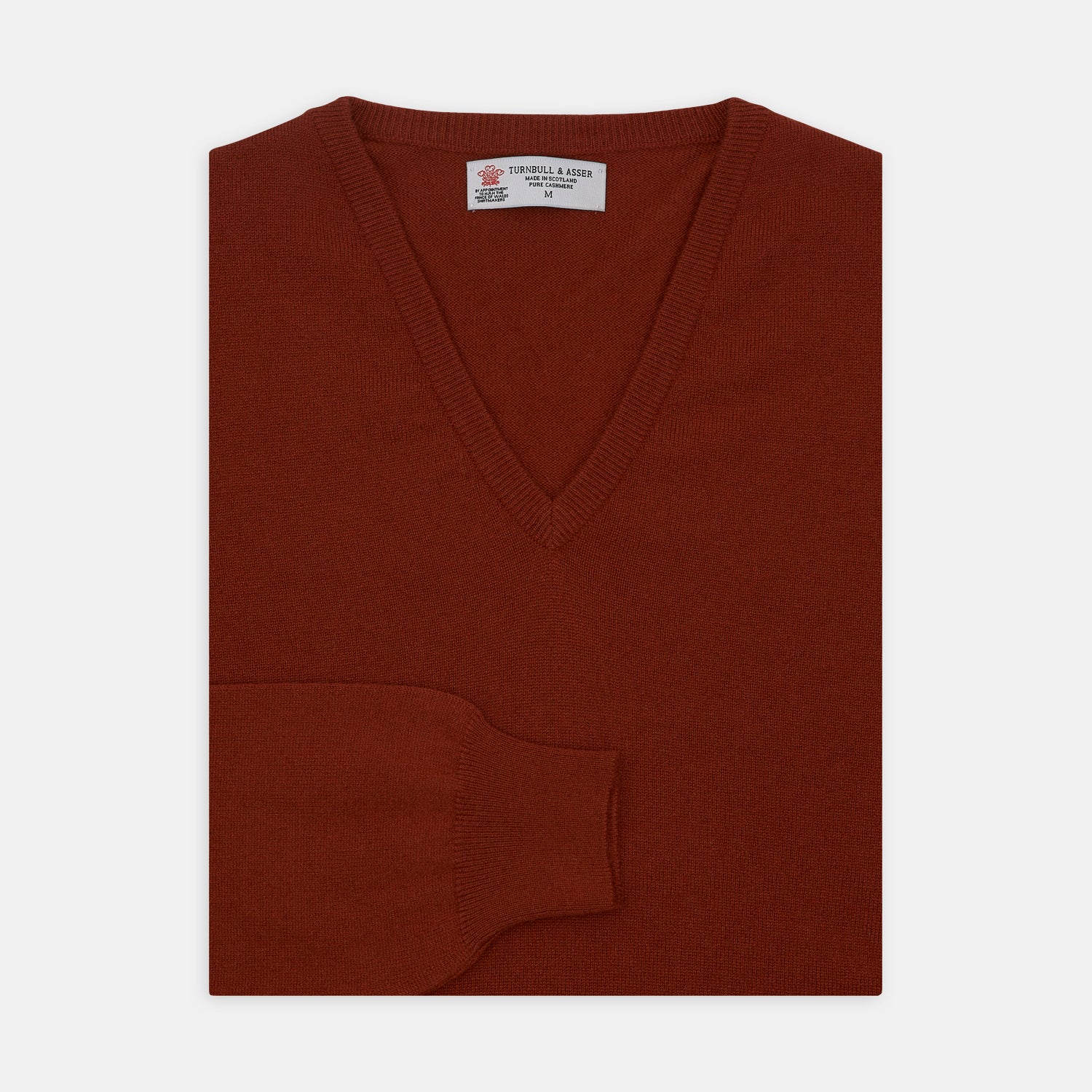 View 1 of product The Turnbull & Asser Harissa V-Neck Cashmere Jumper is shown folded in deep red with ribbed cuffs and a visible collar label, set against a white background.