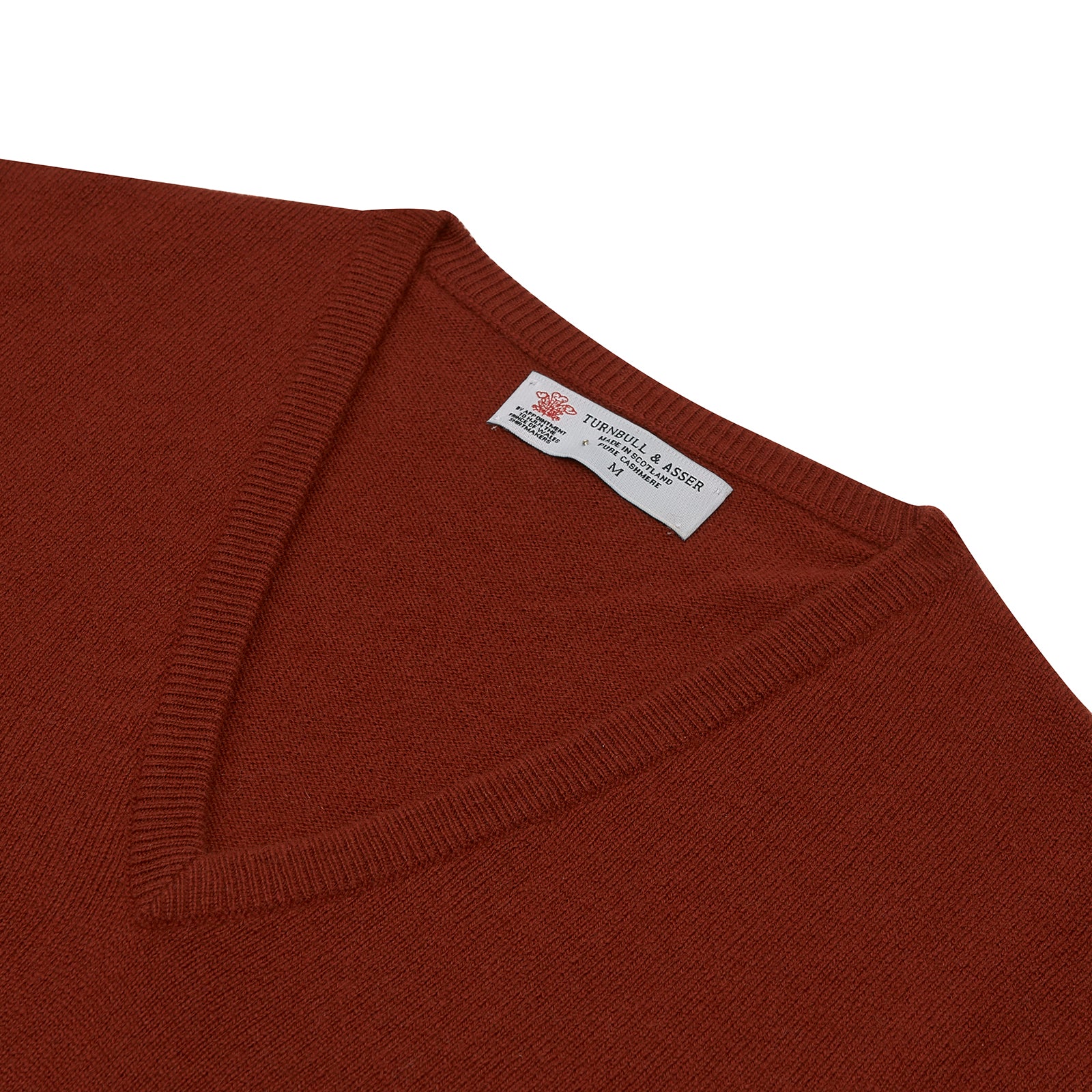 View 2 of product The Turnbull & Asser Harissa V-Neck Cashmere Jumper is shown folded in deep red with ribbed cuffs and a visible collar label, set against a white background.