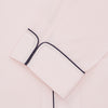 View 2 of product The Pink Sea Island Cotton Pyjama Set by Turnbull & Asser features a folded light pink top with black piping and white buttons, shown beside a matching headscarf with two ties, highlighting luxury men’s sleepwear on a white background.