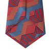 View 4 of product The Turnbull & Asser Red and Blue Zig Zag Silk Tie is a limited-run silk tie featuring interlocking geometric zigzag shapes and diagonal stripes in red, blue, gold, and navy.