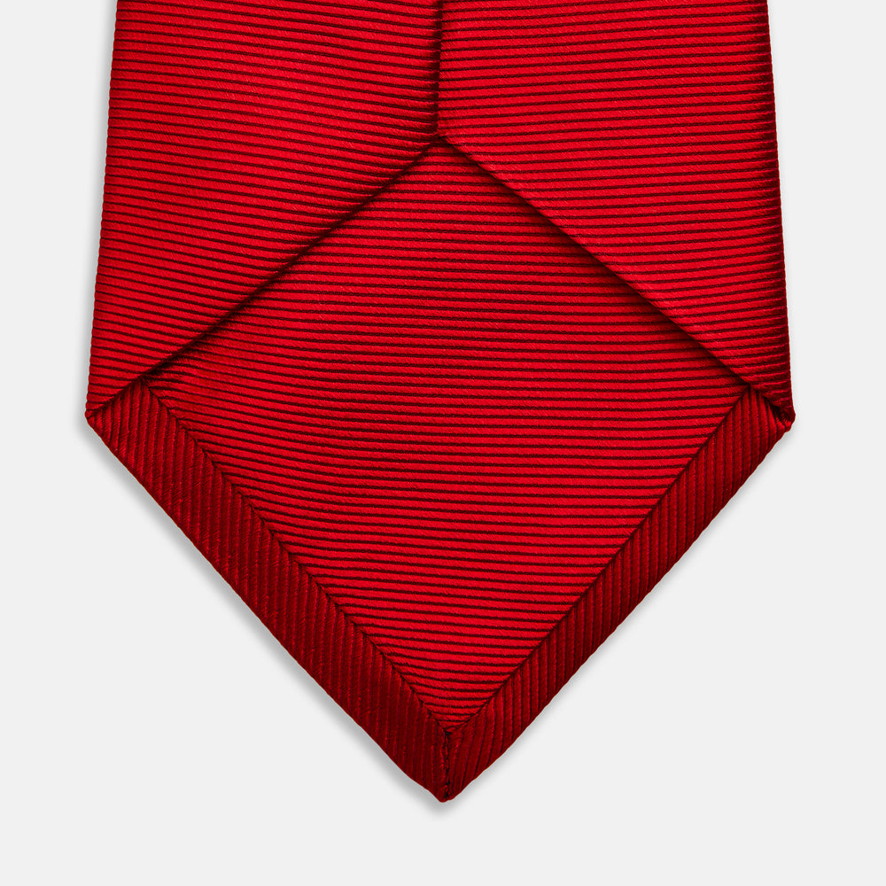 The Turnbull & Asser Red Horizontal Twill Silk Tie, rolled up, is ideal for adding a smart touch to cotton shirts.