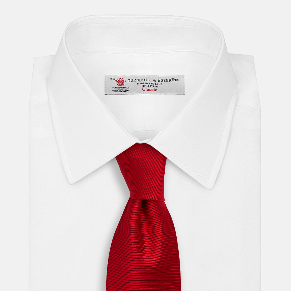 The Turnbull & Asser Red Horizontal Twill Silk Tie, rolled up, is ideal for adding a smart touch to cotton shirts.