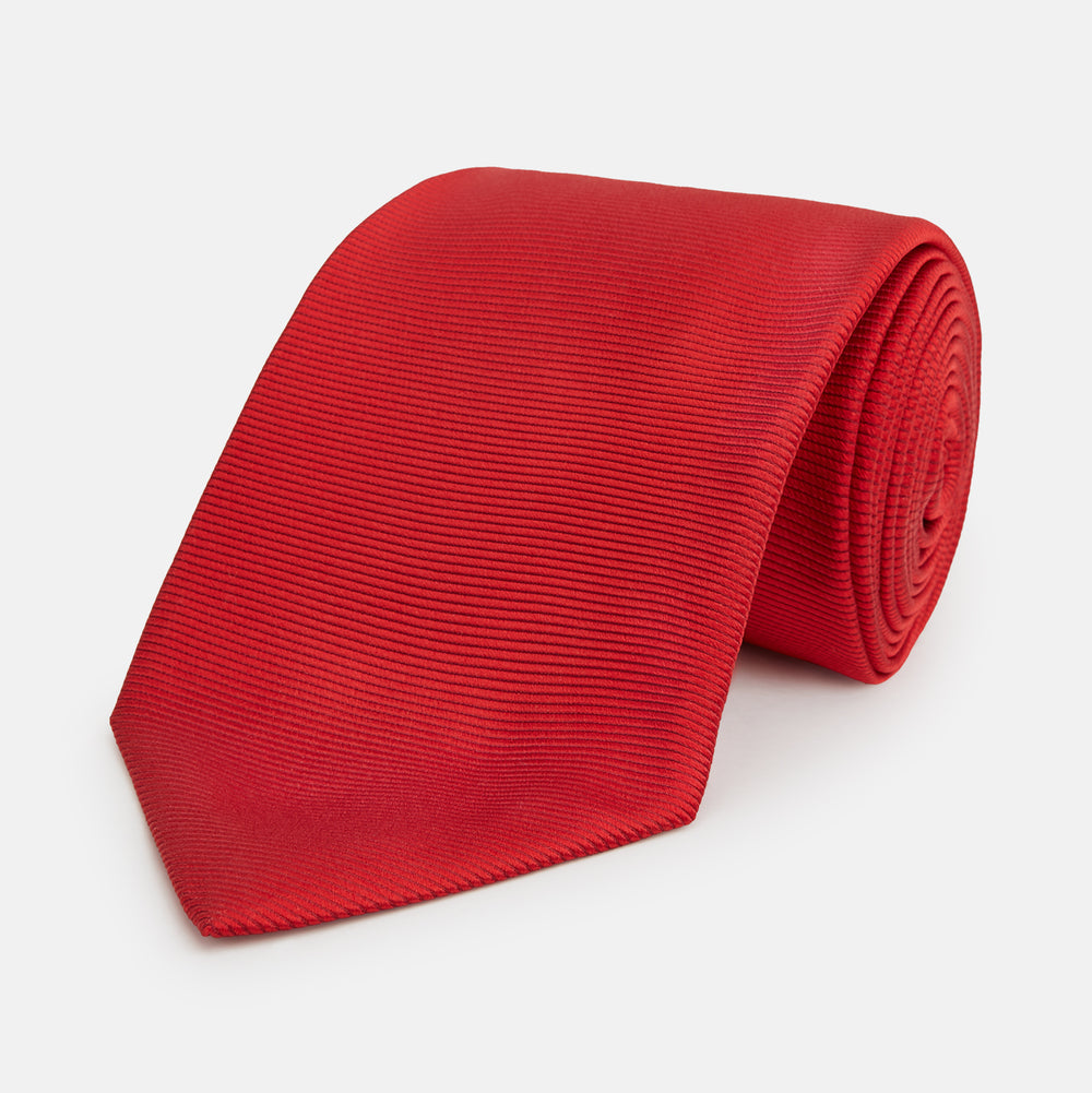 The Turnbull & Asser Red Horizontal Twill Silk Tie, rolled up, is ideal for adding a smart touch to cotton shirts.