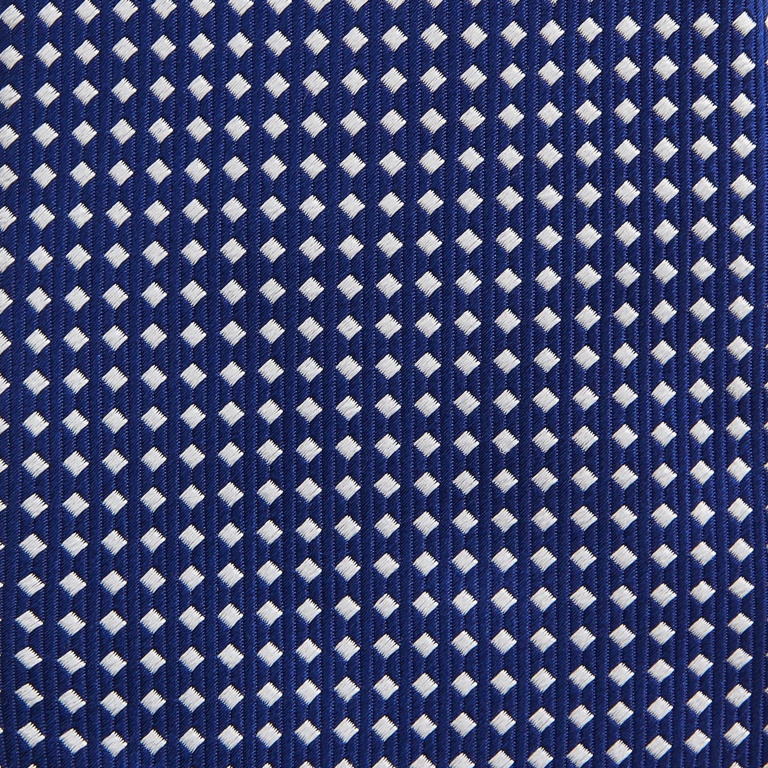 View 3 of product The Turnbull & Asser Slim Diamond Navy and White Silk Tie, featuring a subtle geometric pattern, is rolled up and displayed on a plain white background—ideal for complementing an office shirt.