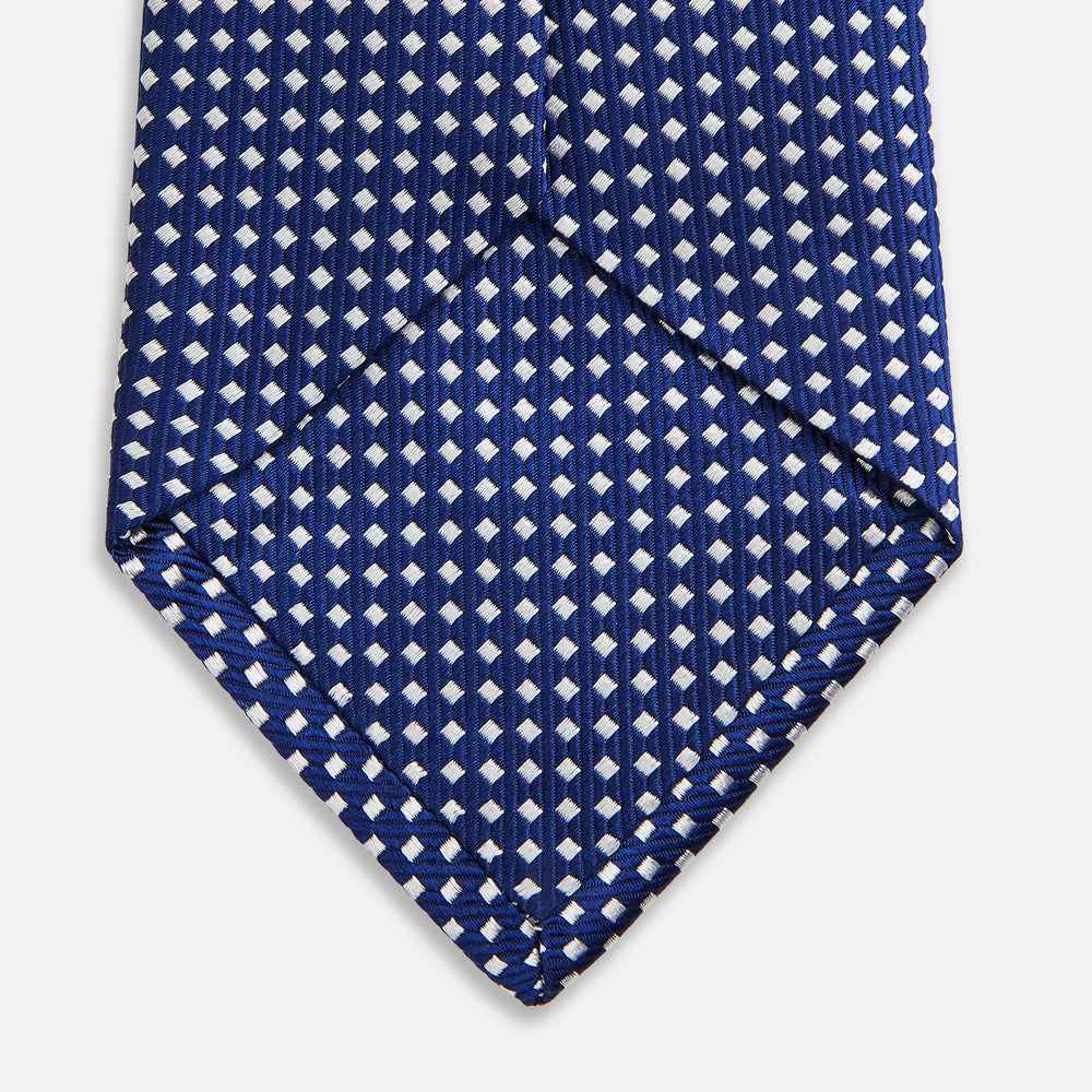 The Turnbull & Asser Slim Diamond Navy and White Silk Tie, featuring a subtle geometric pattern, is rolled up and displayed on a plain white background—ideal for complementing an office shirt.