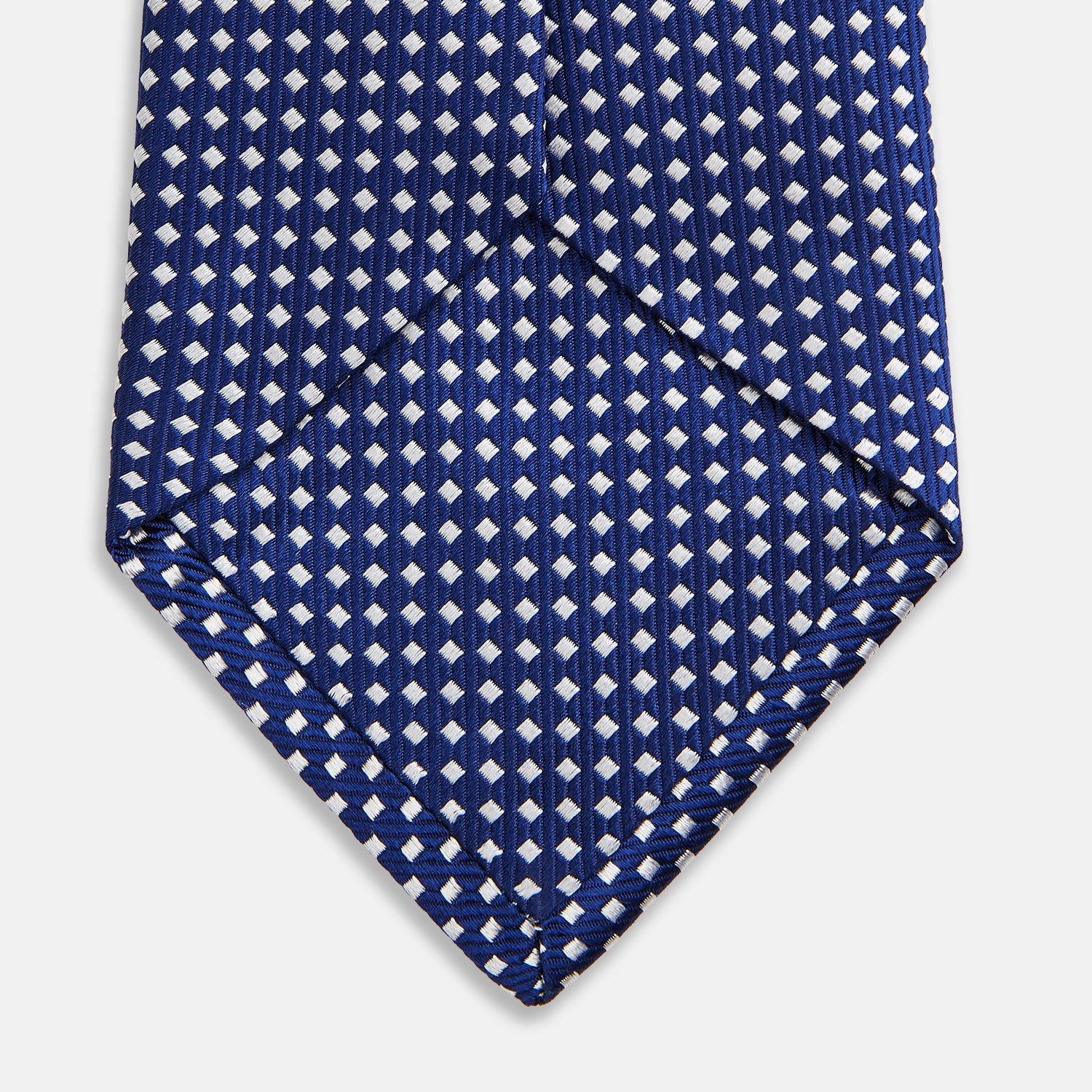 View 4 of product The Turnbull & Asser Slim Diamond Navy and White Silk Tie, featuring a subtle geometric pattern, is rolled up and displayed on a plain white background—ideal for complementing an office shirt.