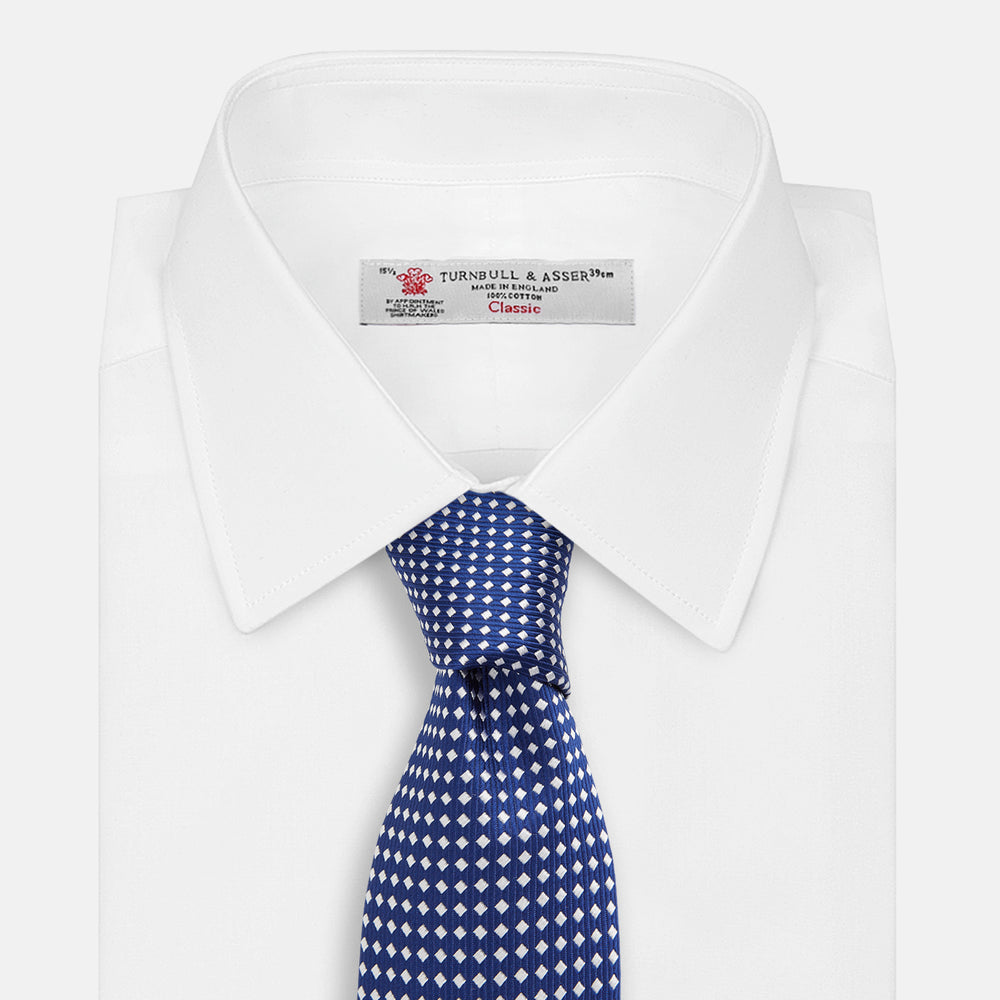 The Turnbull & Asser Slim Diamond Navy and White Silk Tie, featuring a subtle geometric pattern, is rolled up and displayed on a plain white background—ideal for complementing an office shirt.