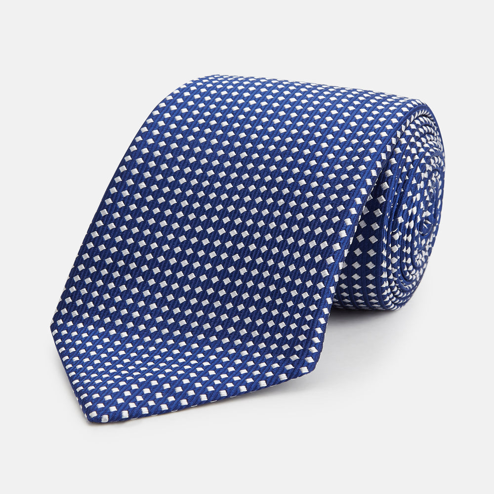 The Turnbull & Asser Slim Diamond Navy and White Silk Tie, featuring a subtle geometric pattern, is rolled up and displayed on a plain white background—ideal for complementing an office shirt.