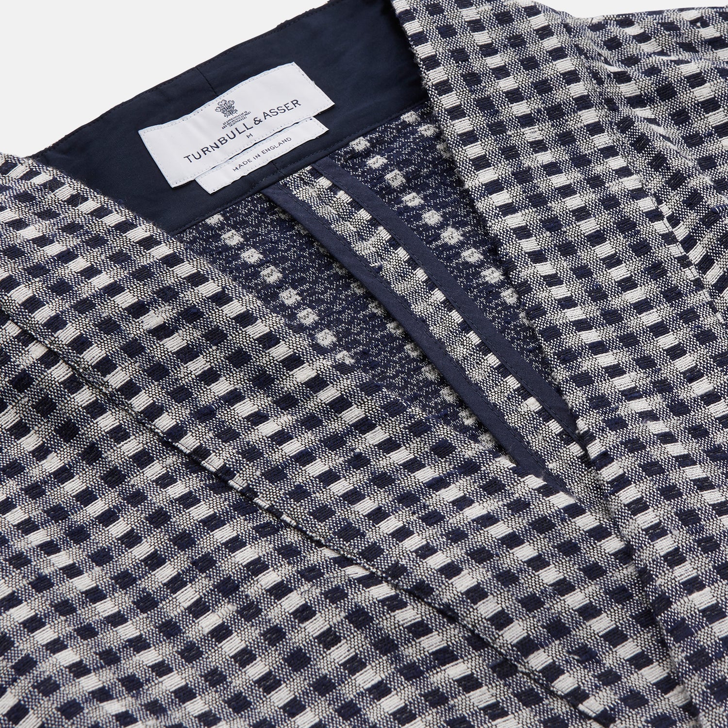 View 5 of product A barefoot person wears Turnbull & Asser's Navy Silk Chequered Kimono Gown with a belt over maroon pyjama sets, standing against a plain light background.
