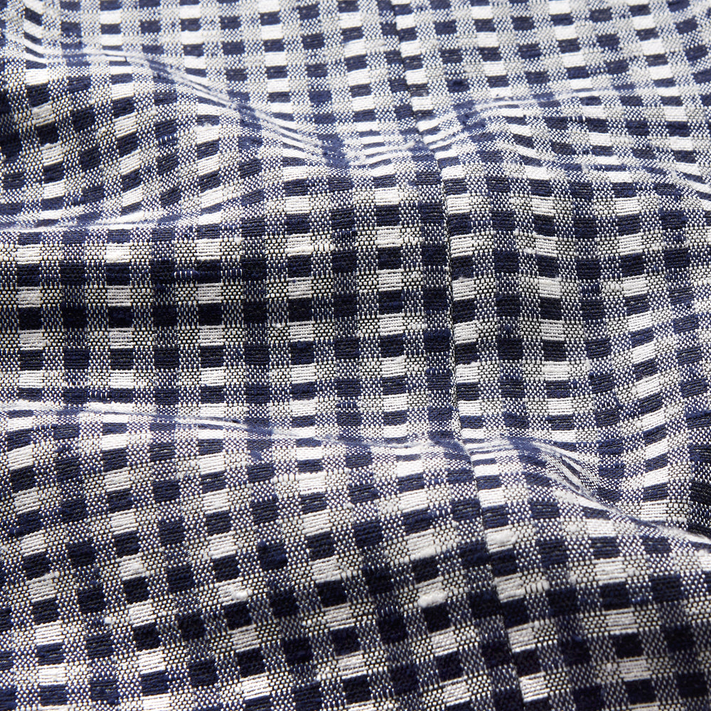 A barefoot person wears Turnbull & Asser's Navy Silk Chequered Kimono Gown with a belt over maroon pyjama sets, standing against a plain light background.