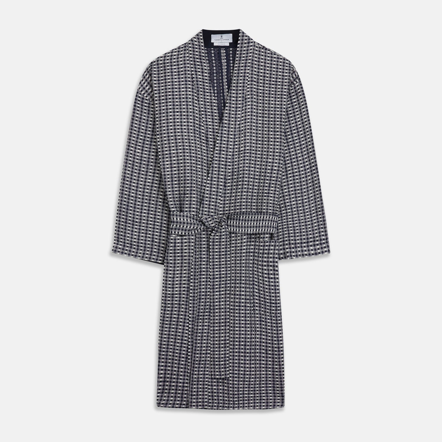 View 2 of product A barefoot person wears Turnbull & Asser's Navy Silk Chequered Kimono Gown with a belt over maroon pyjama sets, standing against a plain light background.