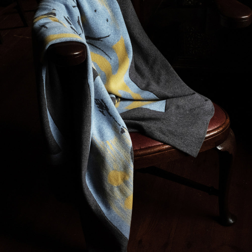 The Pale Blue Wool and Cashmere Lily Blanket by Turnbull & Asser features abstract, hand-drawn designs in blue, yellow, and gray on a white background.