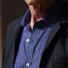 View 1 of product Close-up of a person wearing the Turnbull & Asser Blue Stripe Weekend Fit Nevis Shirt with Derby Collar and 1-Button Cuffs under a dark pinstripe blazer, focusing on the collar and upper chest. The face is partially out of frame.