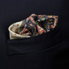 View 3 of product The Cream Paisley Polka Dot Silk Pocket Square by Turnbull & Asser features hand-rolled edges, a detailed blue, red, and yellow paisley design with central orange dots, and the brand's name printed in one corner.