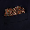 View 3 of product The Orange House Paisley Print Silk Pocket Square by Turnbull & Asser features a brown paisley design on a light brown silk background with a solid brown border and brand's logo printed in one corner.