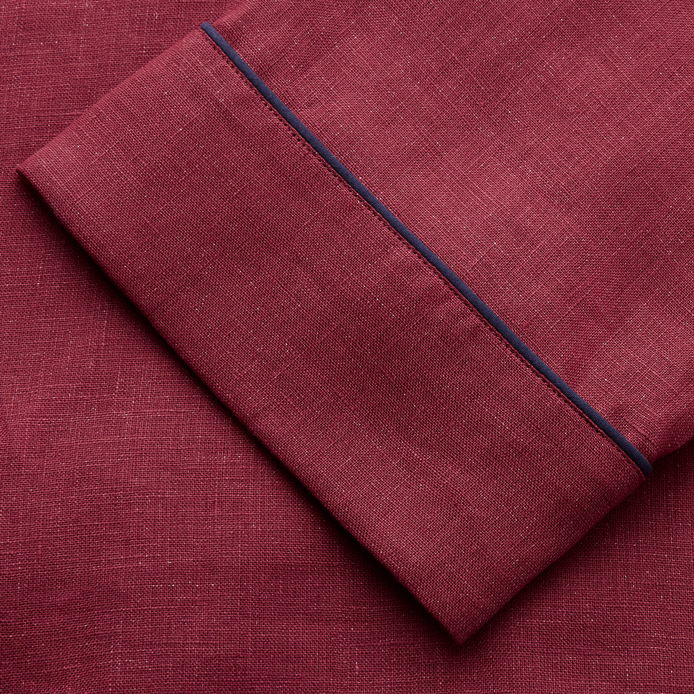 The Turnbull & Asser Burgundy Linen Modern Pyjama Set features a button-up, collared long-sleeve top with black piping and three pockets, plus matching pants with an elastic waistband.
