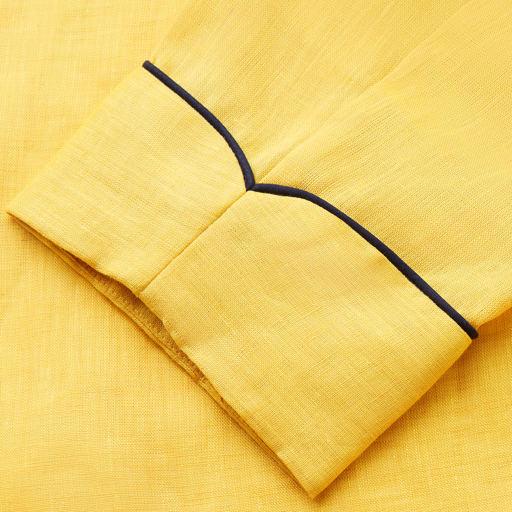 The Turnbull & Asser Ochre Linen Piped Gown features black piping on the collar, cuffs, and edges, a chest pocket, two front pockets, and a matching waist belt. Made with breathable linen for comfort, shown against a plain white background.