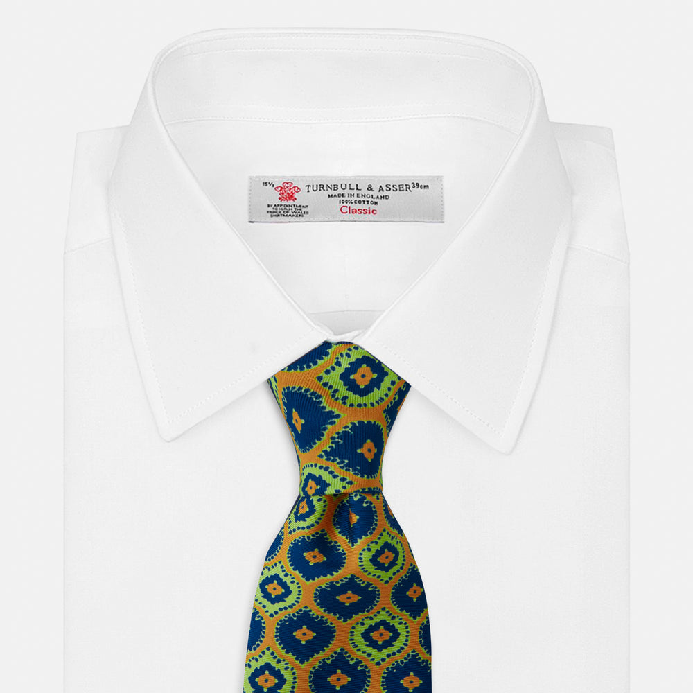 The Yellow Medallion Printed Silk Tie by Turnbull & Asser features a bold abstract medallion pattern in blue, green, and orange on yellow silk, displayed rolled up against a plain white background.
