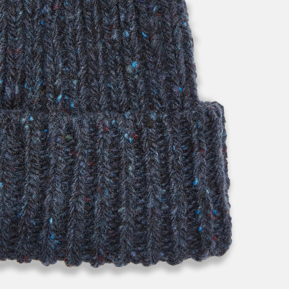 The Turnbull & Asser Navy Donegal Ribbed Merino Hat features thick ribbed knitting, a folded brim, and subtle lighter blue and red flecks throughout the merino yarn, shown against a plain white background.