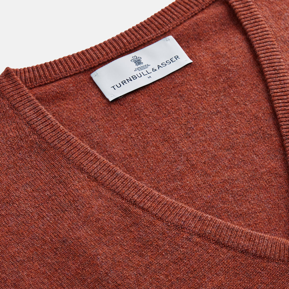 The Turnbull & Asser Burgundy Ifor Cashmere Slipover, a sleeveless V-neck design in fine knit, is shown laid flat on a white background; the neck lining displays a small label, highlighting its Scottish craftsmanship.