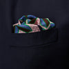 View 3 of product The Pink Multi Crosses Double-Faced Silk Pocket Square by Turnbull & Asser features blue, green, and brown interlocking X-shaped graphics on light pink, with OSINACHI X CJANGO and TURNBULL & ASSER printed at the corners.