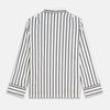View 6 of product A person stands barefoot on a concrete floor, wearing the Turnbull & Asser Black & White Stripe Harriet Women’s Pyjama Set, featuring loose-fitting white pajamas with black vertical stripes, against a plain beige wall in soft side lighting.