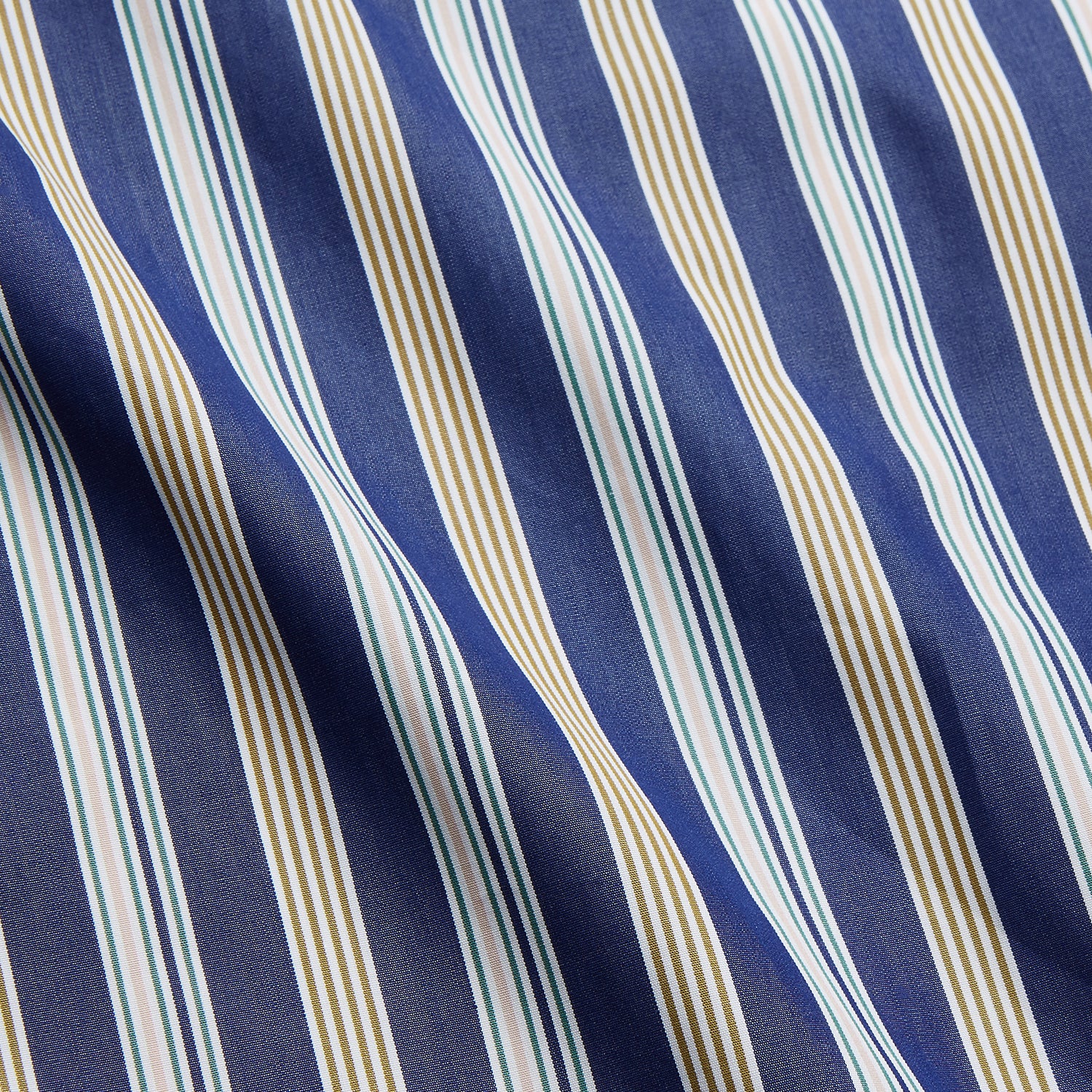 View 4 of product A person stands barefoot on a gray floor in the Turnbull & Asser Blue Multi Stripe Harriet Women’s Pyjama Set with a dark sweater over their shoulders—premium cotton pyjamas that make a perfect gift for her—against a plain beige background.