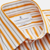 View 4 of product A man stands against a tan background wearing a Turnbull & Asser Orange Multi Stripe Regular Fit Shirt with T&A Collar and 3 Button Cuffs, paired with tan dress pants, brown belt, and brown shoes. He faces forward with a neutral expression.