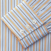 View 4 of product A man stands against a beige background, wearing a Turnbull & Asser Blue, Orange & Navy Multi Stripe Regular Fit Shirt with T&A collar and 3-button cuffs, tucked into tan dress pants with a black belt. He faces forward with a neutral expression.