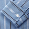 View 4 of product A man stands against a plain tan background wearing Turnbull & Asser's Blue Multi Chambray Stripe Weekend Fit Shirt with a Derby collar and 1 button cuffs, paired with a red patterned tie and gray trousers. His hands are in his pockets.