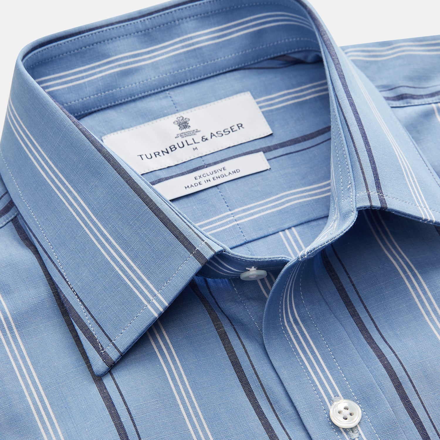 View 3 of product A man stands against a plain tan background wearing Turnbull & Asser's Blue Multi Chambray Stripe Weekend Fit Shirt with a Derby collar and 1 button cuffs, paired with a red patterned tie and gray trousers. His hands are in his pockets.