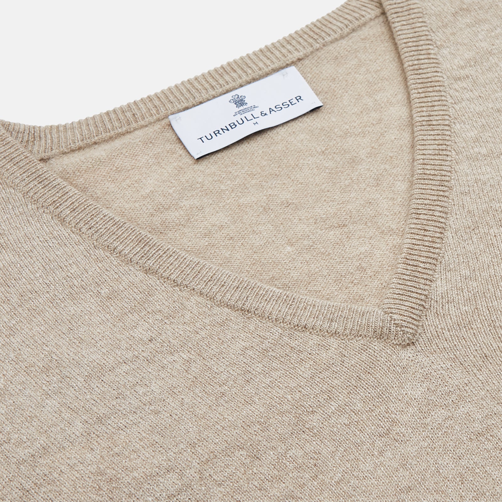 View 2 of product The Turnbull & Asser Beige Cashmere Paden V-Neck Jumper is laid flat on a white background. Knitted in Scotland, this men's staple features ribbed cuffs, hem, and neckline with a soft, smooth texture.