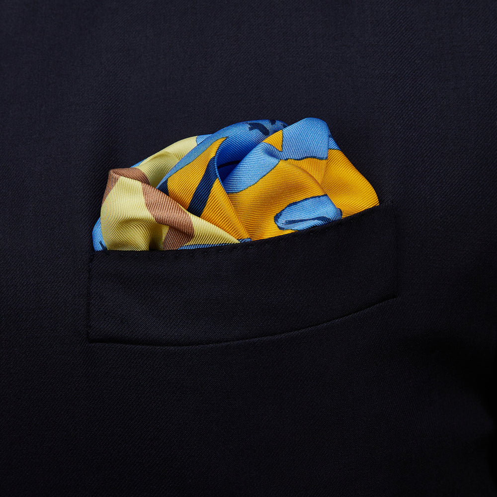 The Blue and Yellow Lily Silk Pocket Square by Turnbull & Asser features a vibrant, hand-drawn design of large blue lilies with dark stems on a yellow background adorned with pale blue stripes and tan abstract shapes.