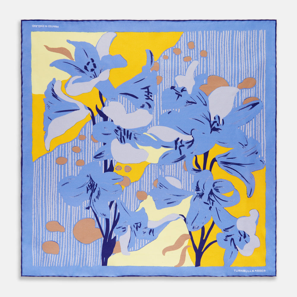 The Blue and Yellow Lily Silk Pocket Square by Turnbull & Asser features a vibrant, hand-drawn design of large blue lilies with dark stems on a yellow background adorned with pale blue stripes and tan abstract shapes.