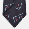View 3 of product A Turnbull & Asser Navy Graphic Deco Silk Tie, featuring light blue chevrons and red squares on a dark navy background, shown rolled up against a plain white backdrop.