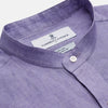 View 5 of product A man stands against a beige background wearing the Turnbull & Asser Lilac Weekend Fit Linen Blake Shirt with Stand Collar and 1-Button Cuffs, paired with dark pinstriped pants and brown sandals—a relaxed weekend look.