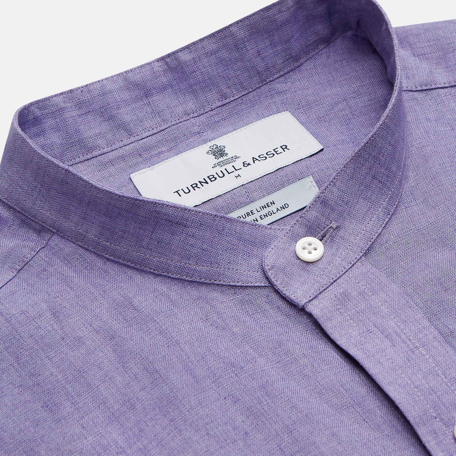 View 5 of product A man stands against a beige background wearing the Turnbull & Asser Lilac Weekend Fit Linen Blake Shirt with Stand Collar and 1-Button Cuffs, paired with dark pinstriped pants and brown sandals—a relaxed weekend look.