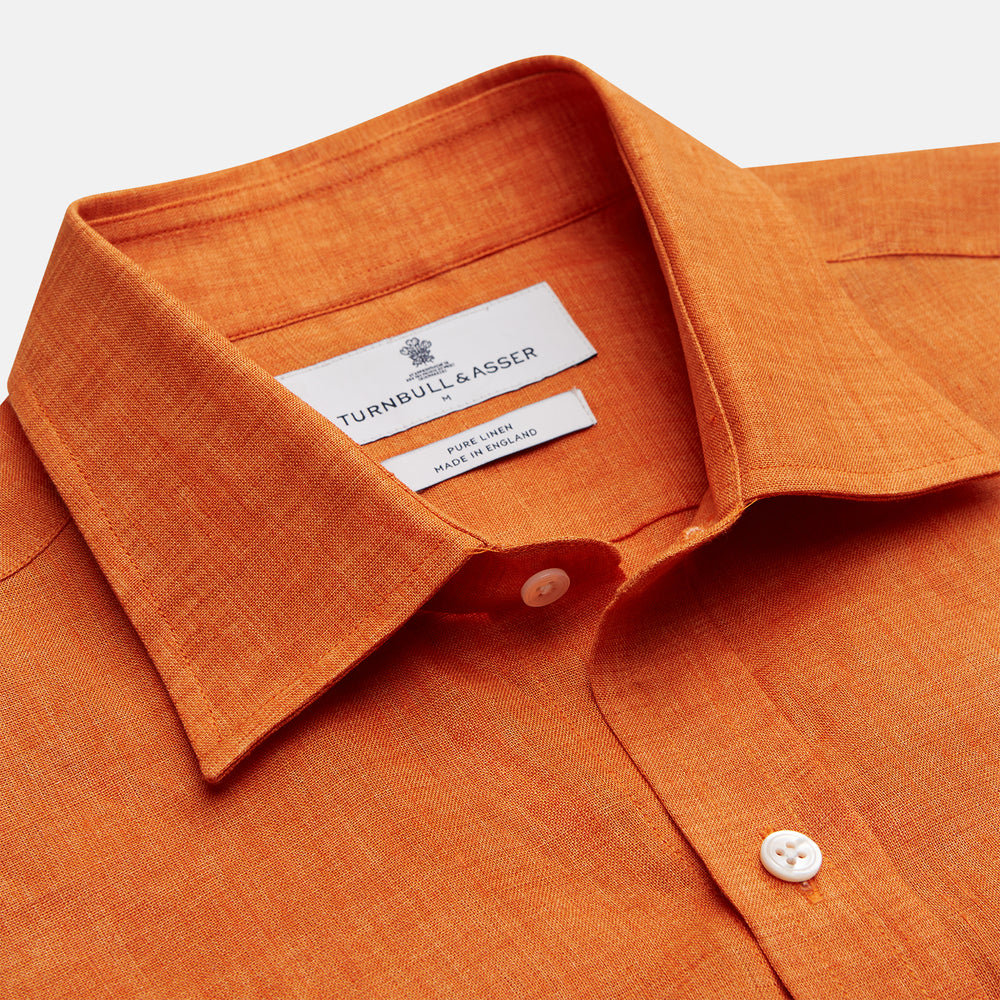 The Turnbull & Asser Orange Weekend Fit Linen Nevis Shirt features a Derby collar, long sleeves with 1-button cuffs, white buttons, and a chest pocket, shown flat against a white background.