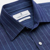 View 3 of product Close-up of a person wearing the Turnbull & Asser Blue Stripe Weekend Fit Nevis Shirt with Derby Collar and 1-Button Cuffs under a dark pinstripe blazer, focusing on the collar and upper chest. The face is partially out of frame.