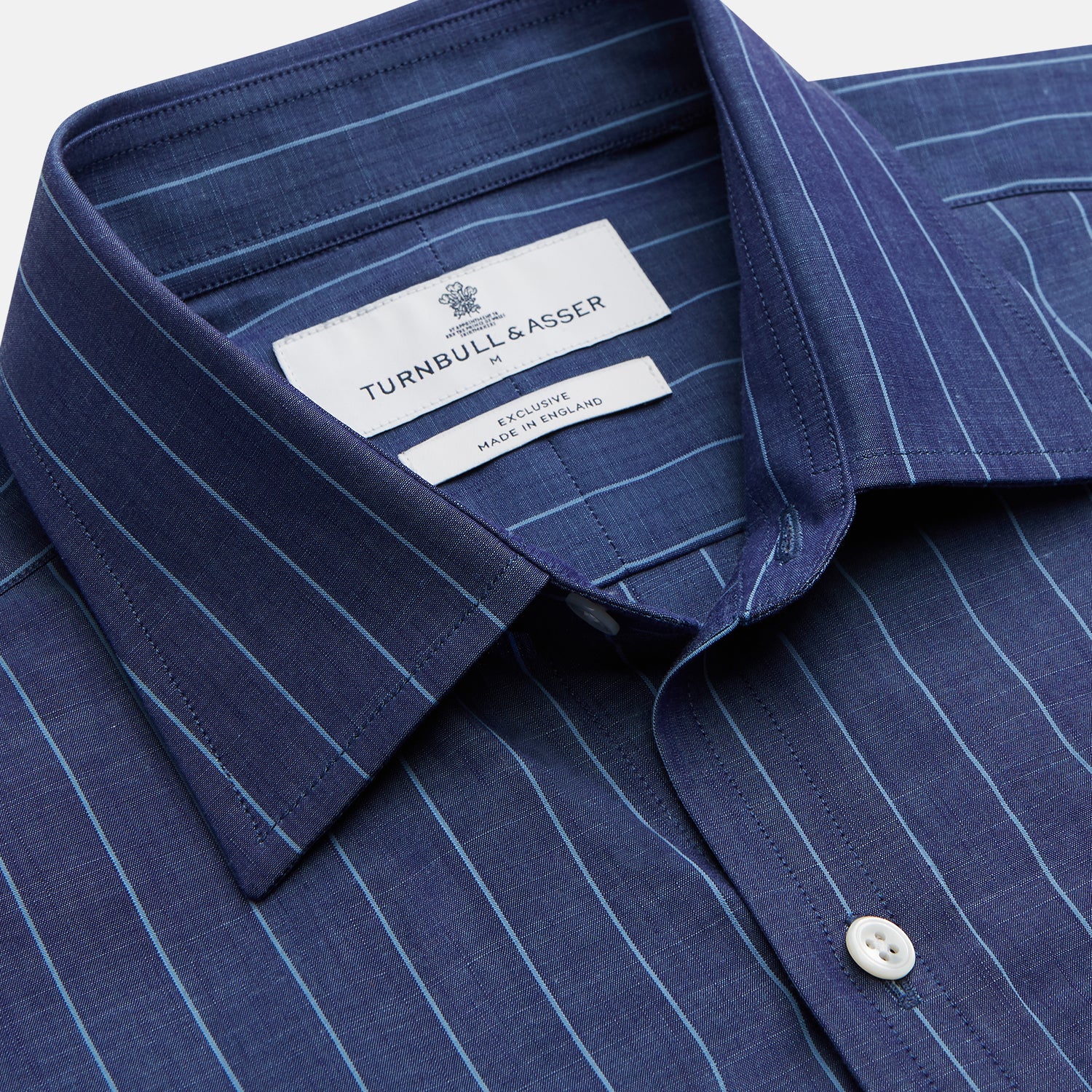 View 3 of product Close-up of a person wearing the Turnbull & Asser Blue Stripe Weekend Fit Nevis Shirt with Derby Collar and 1-Button Cuffs under a dark pinstripe blazer, focusing on the collar and upper chest. The face is partially out of frame.