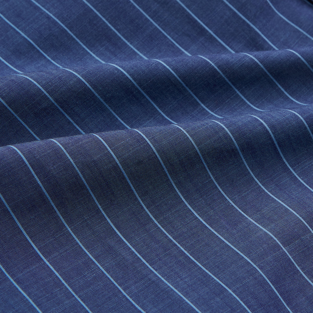 Close-up of a person wearing the Turnbull & Asser Blue Stripe Weekend Fit Nevis Shirt with Derby Collar and 1-Button Cuffs under a dark pinstripe blazer, focusing on the collar and upper chest. The face is partially out of frame.
