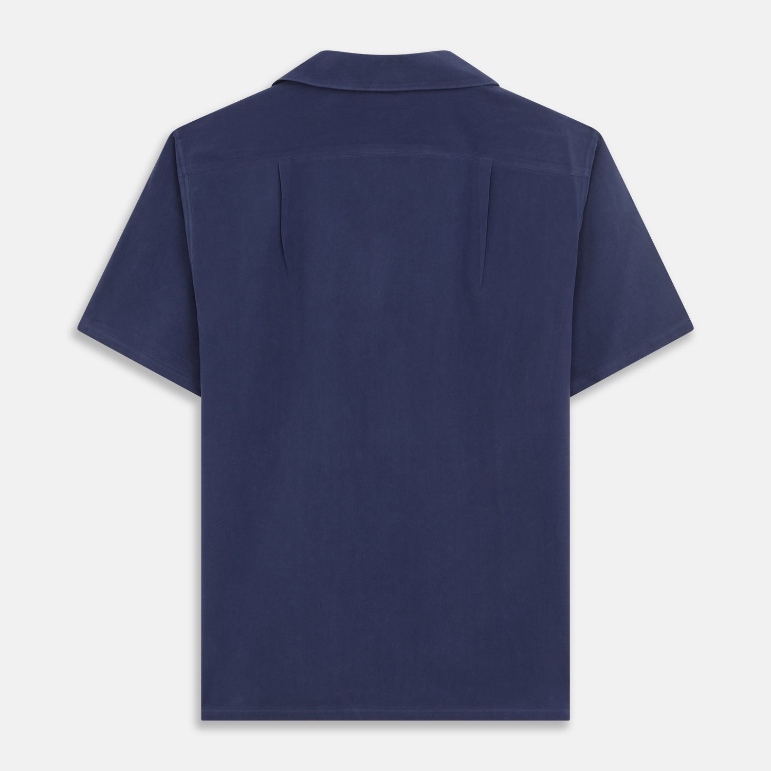 View 5 of product A man stands against a beige backdrop, wearing the Turnbull & Asser Navy Holiday Fit Silk Phillips Shirt with Revere Collar and dark pinstripe pants. He gazes downwards with a relaxed expression, embodying effortless summer style.