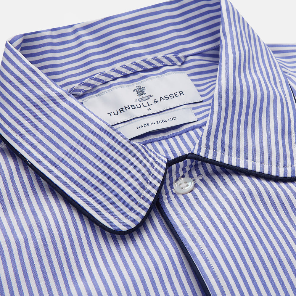 The Turnbull & Asser Blue Bengal Stripe Piped Cotton Nightshirt features long sleeves, a pointed collar, dark-trimmed pocket, curved hem, button details, and cuffed sleeves for an elegant look.