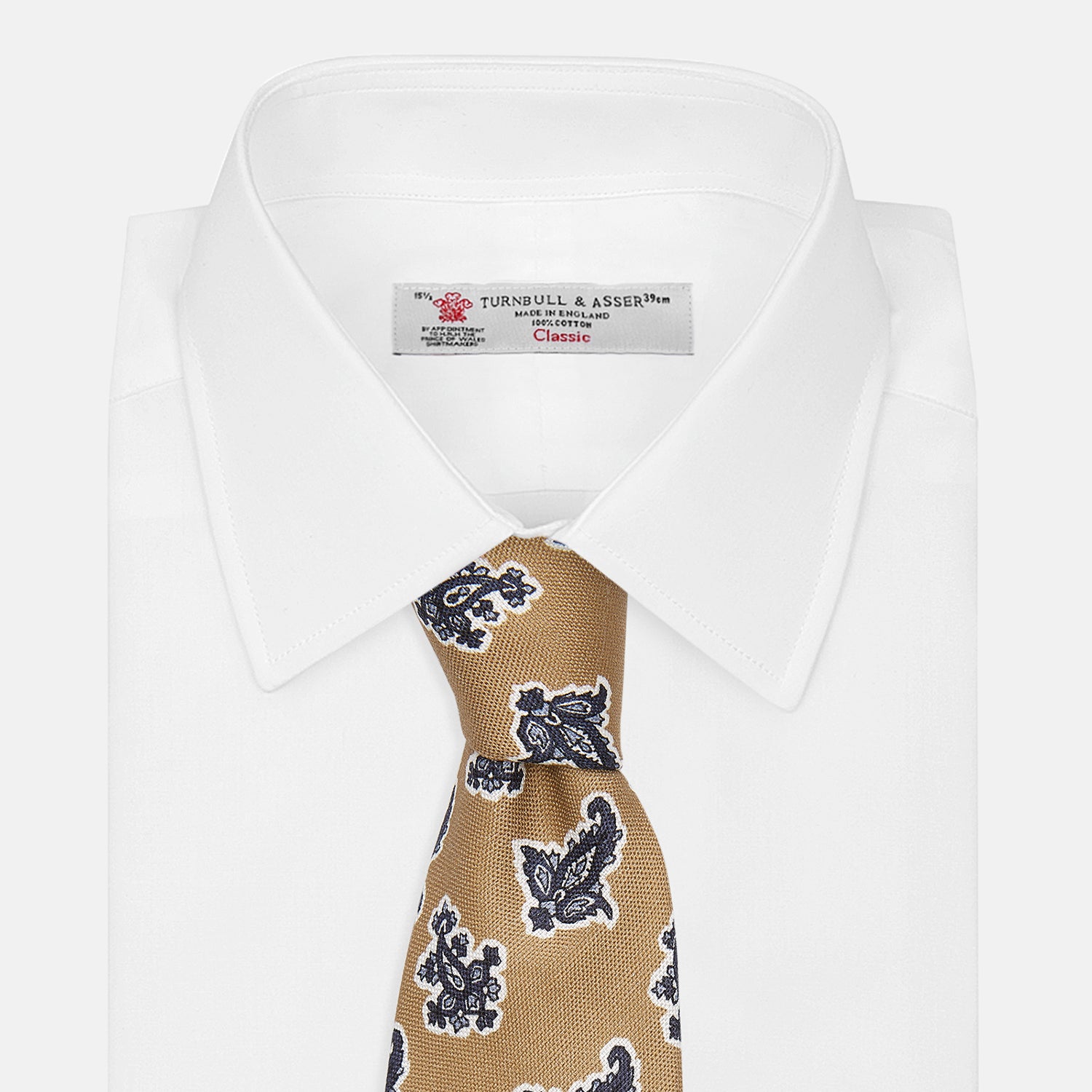 View 4 of product The Turnbull & Asser Toffee Paisley Floral Cotton Silk Blend Tie features a rolled-up design with dark blue and white paisley motifs on a tan background.