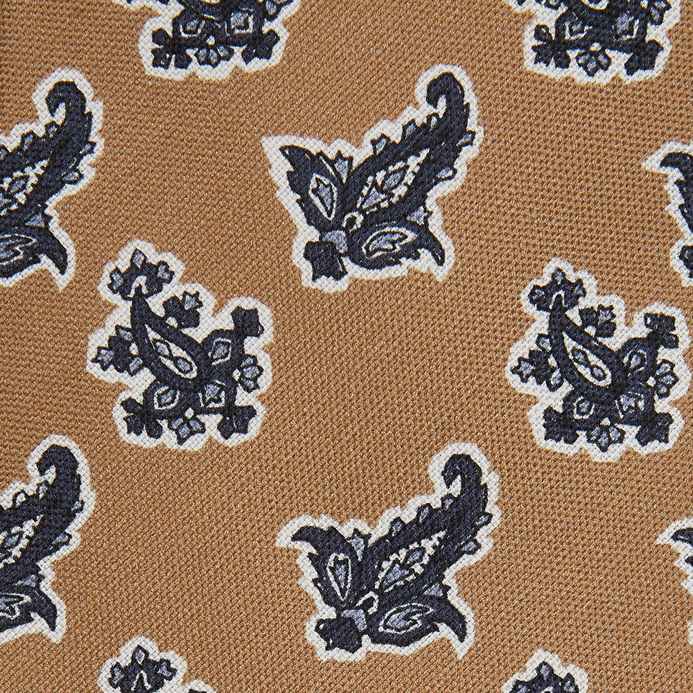 The Turnbull & Asser Toffee Paisley Floral Cotton Silk Blend Tie features a rolled-up design with dark blue and white paisley motifs on a tan background.