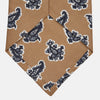 View 3 of product The Turnbull & Asser Toffee Paisley Floral Cotton Silk Blend Tie features a rolled-up design with dark blue and white paisley motifs on a tan background.
