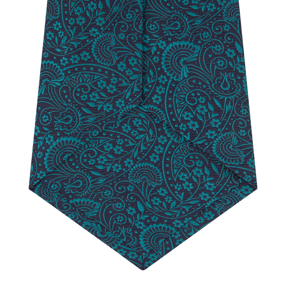 The Turnbull & Asser Green and Navy Tonal Paisley Silk Tie is an elegant men's accessory, featuring a rolled-up design with an intricate paisley pattern, shown on a white background.